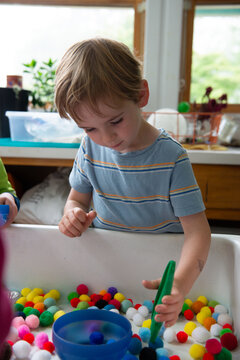 Child uses tweezers at a sensory table in a preschool classroom