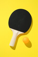 Ping pong racket and ball on yellow background, top view