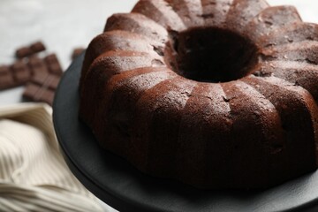 Tasty bundt cake and pieces of chocolate on table, closeup