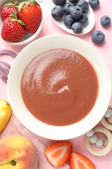 Baby food. Tasty puree in bowl, teether and ingredients on pink background, flat lay