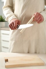 Man sharpening knife with sharpener at beige table indoors, closeup