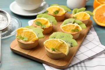 Tartlets with fruits and mint on light blue wooden table, closeup. Delicious dessert