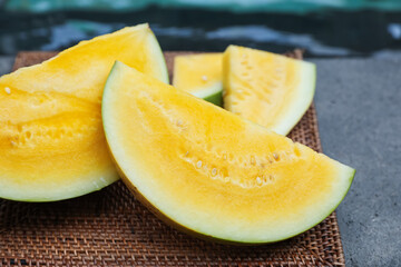 Pieces of ripe yellow watermelon on wicker table near swimming pool, closeup