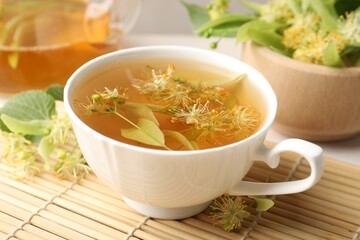 Fresh linden tea in cup, teapot and flowers on table, closeup