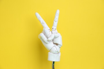 White mannequin hand showing peace sign on yellow background