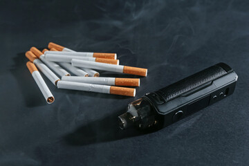 Electronic smoking device and cigarettes in smoke on dark table, closeup