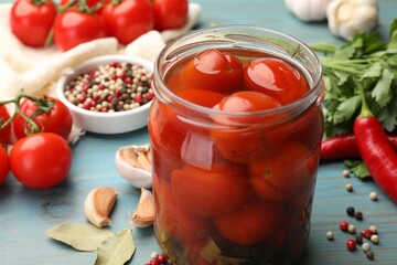 Tasty pickled tomatoes in jar and ingredients on light blue wooden table, closeup