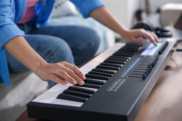 Woman working with MIDI keyboard at table indoors, closeup