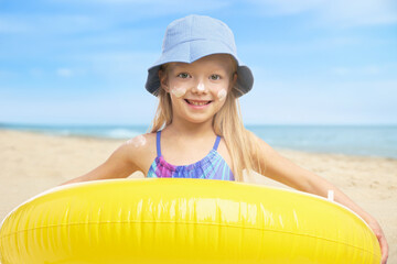 Cute little girl with sunscreen on her skin holding inflatable ring at beach. Sun protection while...