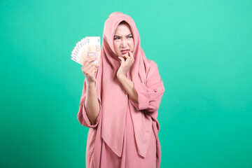 Pensive young woman in hijab holds euro bills, expressing financ