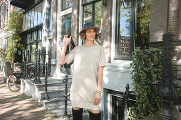 Horizontal photo of beautiful elegant woman wearing fashionable outfit, holding jacket behind the back in front of typical Dutch building of Amsterdam city - Tourist enjoying summer vacation Europe 