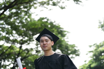 A joyful graduate in a black cap and gown proudly raises his diploma with excitement, looking...