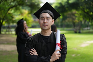 A joyful graduate in a black cap and gown proudly raises his diploma with excitement, looking...