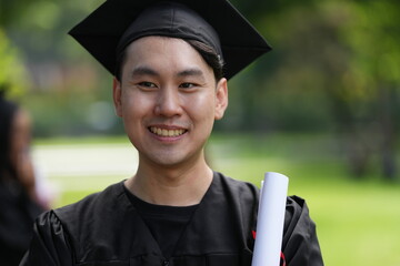 A joyful graduate in a black cap and gown proudly raises his diploma with excitement, looking...