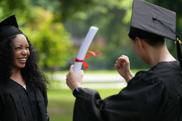 Two graduates in caps and gowns joyfully celebrate, each holding a diploma with smiles and raised...