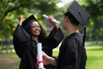 Two graduates in caps and gowns joyfully celebrate, each holding a diploma with smiles and raised...