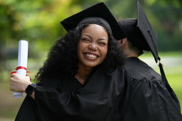Two graduates in caps and gowns joyfully celebrate, each holding a diploma with smiles and raised...
