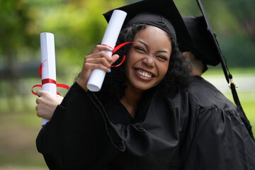 Two graduates in caps and gowns joyfully celebrate, each holding a diploma with smiles and raised...