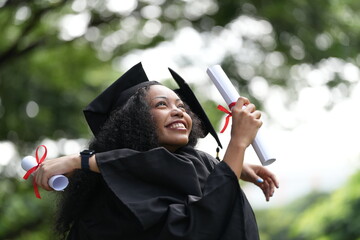 Two graduates in caps and gowns joyfully celebrate, each holding a diploma with smiles and raised...