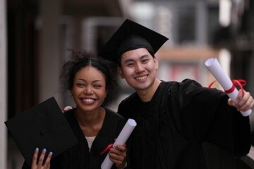 Two graduates in caps and gowns beam with joy, embracing and cheering in celebration. Their wide...
