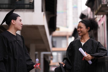Two graduates in caps and gowns beam with joy, embracing and cheering in celebration. Their wide...