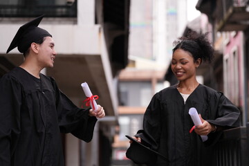 Two graduates in caps and gowns beam with joy, embracing and cheering in celebration. Their wide...