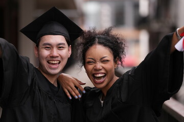 Two graduates in caps and gowns beam with joy, embracing and cheering in celebration. Their wide...