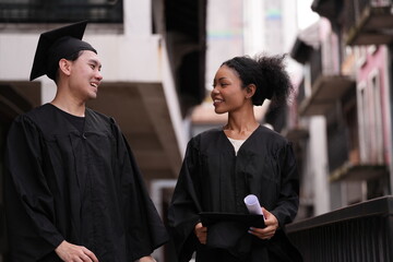 Two graduates in caps and gowns beam with joy, embracing and cheering in celebration. Their wide...