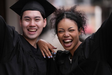 Two graduates in caps and gowns beam with joy, embracing and cheering in celebration. Their wide...