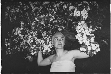 A woman stands among blossoming branches of an apple tree