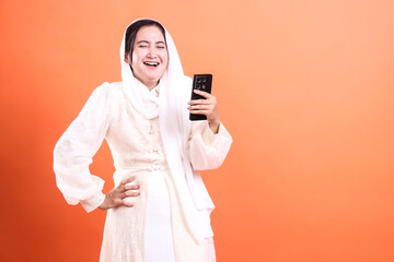 Cheerful Muslim Woman Enjoying Mobile Content: A portrait of a joyful woman in hijab, captivated by...