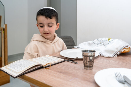 Smiling boy at Shabbat table with prayer book and challah