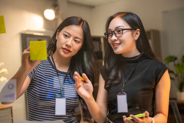 Two women are smiling and holding up a yellow sticky note