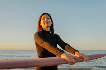 Surfer woman wearing sunscreen preparing for surfing at sunset