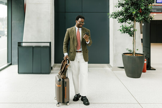 Businessman with Luggage Using Phone in Modern Airport Terminal