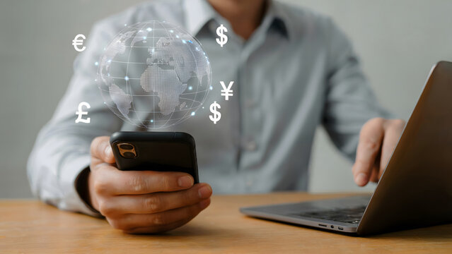 Person using smartphone and laptop for global finance showing currency symbols and world hologram indicating investment, trading, online banking, and digital money transfer. - Powered by Adobe