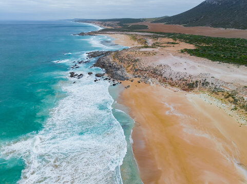Waves breaking onto sandy beach and rocky outcrop