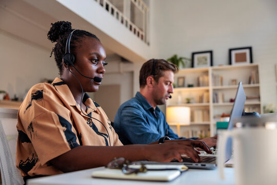 Two people working at computers with headsets on.