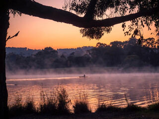 A lone kayak and ducks on a misty morning with mist rising from the lake at sunrise,  with reeds in...