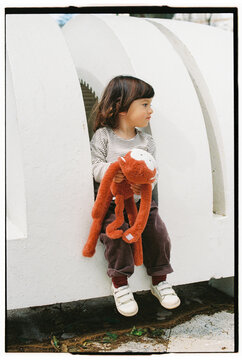 Child Sitting with Red Plush Toy Looking Aside
