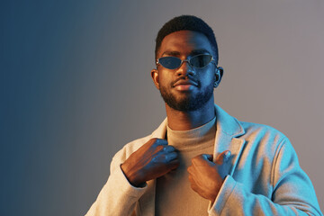 Stylish young man in sunglasses wearing a beige coat and turtleneck against a modern gradient background, exuding confidence and elegance