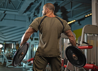 male athlete is engaged in weightlifting at a gym, holding heavy plates in each hand while...