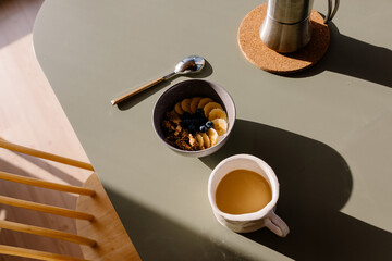 Overhead detail of a bowl of fruit and a coffee on a sunlit table