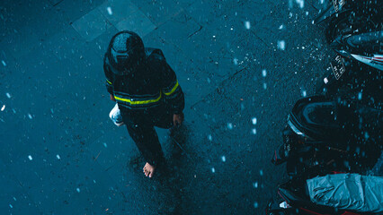 Overhead view of a person walking barefoot through heavy rain on a dark, wet urban street, with...