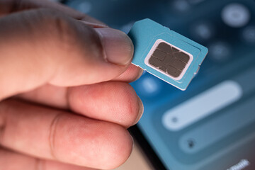 Hand holding a SIM card with blurred smartphone