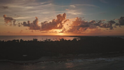 The setting sun warm glow over Rangiroa island in French Polynesia, illuminating sailboats anchored near shore creating a breathtaking aerial view of paradise. Remote wild nature, exotic summer travel