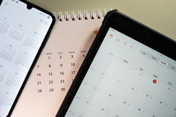Flatlay of smartphone and tablet displaying digital calendars beside a paper calendar