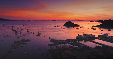 Aerial view of Ende Port in Flores Island, Indonesia, showing boats sailing on the sea during a vibrant and colorful sunset, with islands and mountains in the background