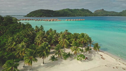 Pristine white sand beach with turquoise water, lush palm trees, and overwater bungalows creating...