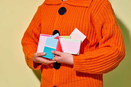 A person holds a collection of colorful notes wearing orange shirt